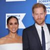 Meghan Markle pictured in a white dress and golden earrings alongside Prince Harry at an event