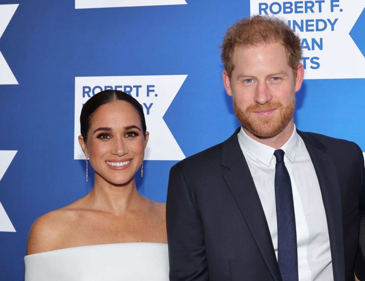 Meghan Markle pictured in a white dress and golden earrings alongside Prince Harry at an event
